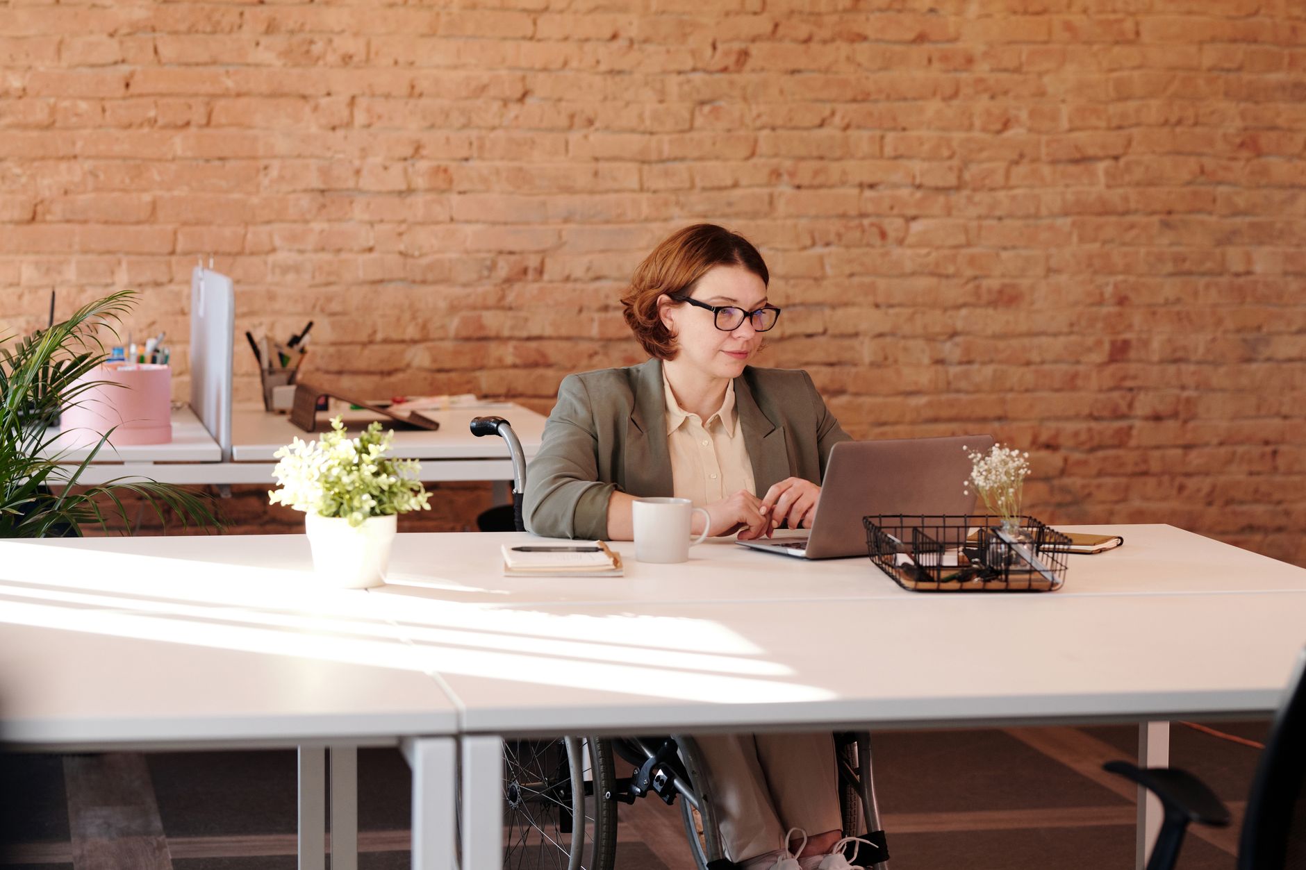 A businesswoman who uses a wheelchair works on a laptop at a desk in a modern office